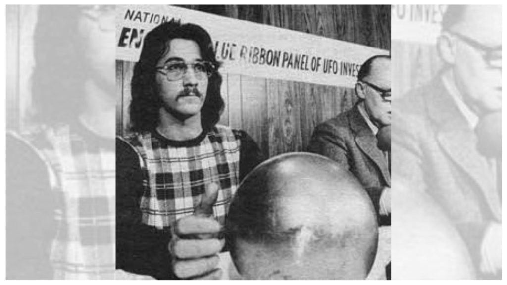 Sculptor James Durling-Jones giving a thumbs up while holding a metal sphere in front of a "Blue Ribbon Panel of UFO Investigators" banner in 1974